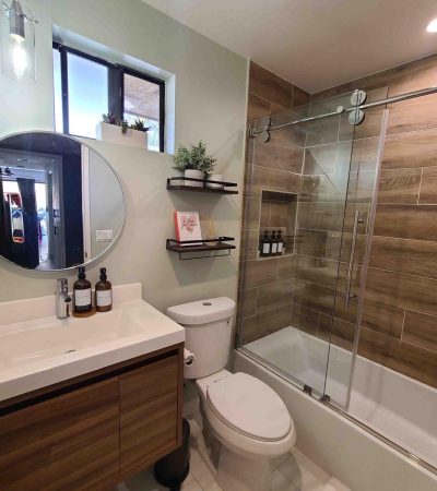 Modern bathroom remodel with wood tile shower, glass doors, floating vanity, round mirror, clean design, and natural light.